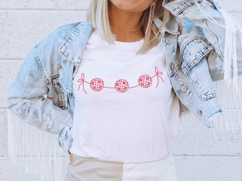 May include: White t-shirt with a pink graphic of a string of disco balls.