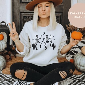 May include: A white sweatshirt with a graphic of two skeletons dancing with cacti and stars. The text "SVG - EPS - DXF - PNG - JPG" is in the upper right corner of the image.
