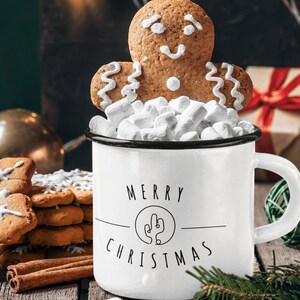 May include: White enamel mug with black trim and the text "Merry Christmas" with a stylised cactus design. The mug is filled with marshmallows and topped with a gingerbread man cookie.
