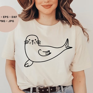 May include: A white t-shirt with a black line drawing of a seal on the front. The seal is facing left and has a simple, cartoon-like design.