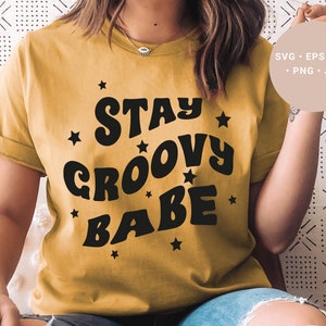May include: A mustard yellow t-shirt with the text "Stay Groovy Babe" in black, retro-style lettering. The text is surrounded by small black stars.