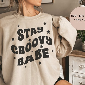 May include: A beige sweatshirt with the text "Stay Groovy Babe" in black with stars around the text.