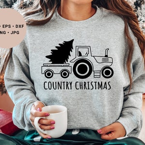 Könnte beinhalten: Ein graues Sweatshirt mit einer schwarz-weißen Illustration eines Traktors, der einen Weihnachtsbaum zieht. Der Text "COUNTRY CHRISTMAS" ist unter der Illustration gedruckt.