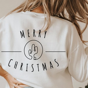 May include: White sweatshirt with the text "Merry Christmas" and a line drawing of a cactus in a circle.