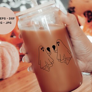 May include: A glass jar containing a brown beverage. The jar features a black and white illustration of two ghosts holding broken hearts. A straw protrudes from the top of the jar.