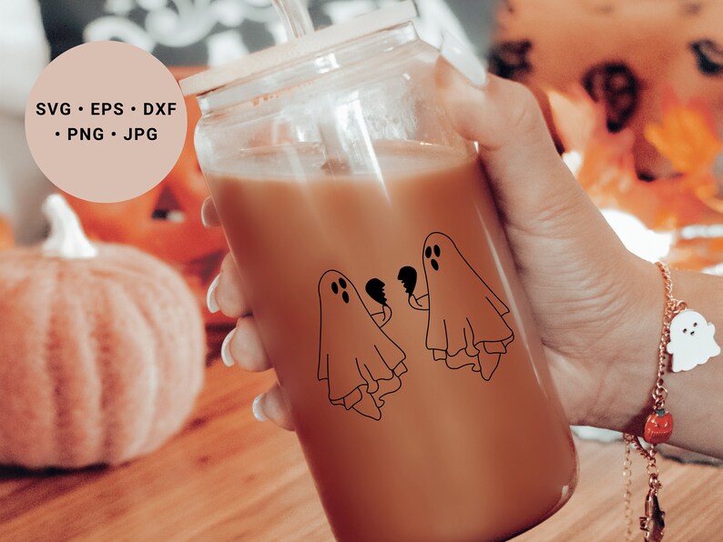 May include: A glass jar containing a brown beverage. The jar features a black and white illustration of two ghosts holding broken hearts. A straw protrudes from the top of the jar.