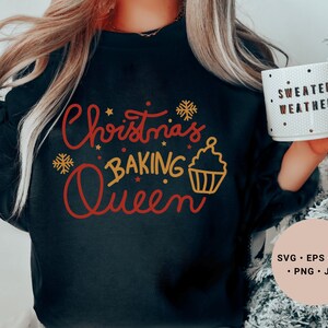 Könnte beinhalten: Ein schwarzes Sweatshirt mit dem Text "Christmas Baking Queen" in roten und goldenen Buchstaben. Der Text ist von Schneeflocken und einer Cupcake-Grafik umgeben. Das Sweatshirt wird von einer Person getragen, die eine weiße Tasse mit dem Text "Sweater Weather" in schwarzen Buchstaben hält.
