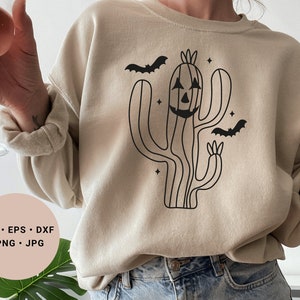 May include: A beige sweatshirt featuring a black outline of a cactus with a jack-o'-lantern face and bats flying around it. The text "SVG - EPS - DXF - PNG - JPG" is on a pink circle in the bottom left corner of the image.