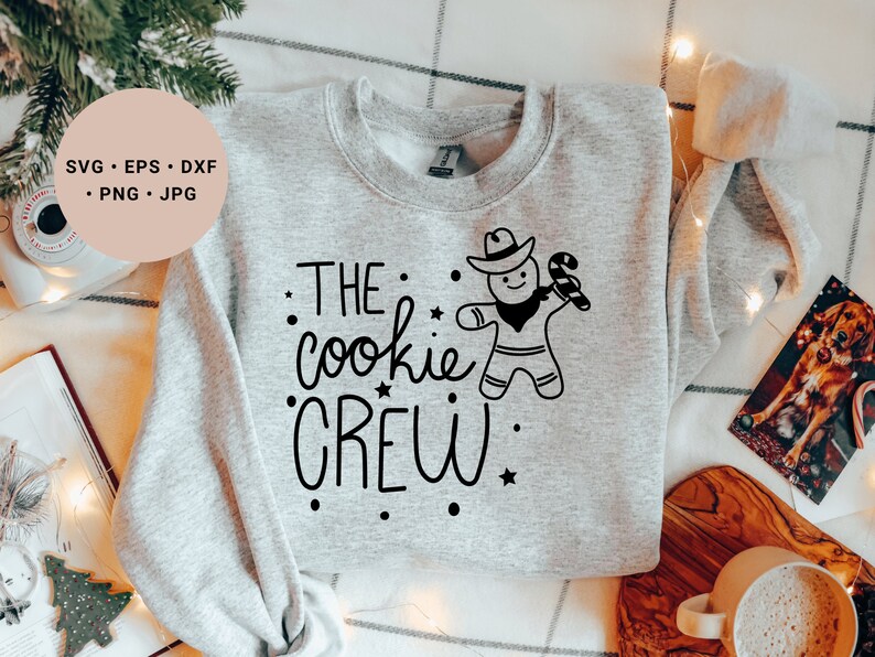 May include: A gray sweatshirt with the text "THE cookie CREW" in black lettering. A gingerbread man wearing a cowboy hat and holding a candy cane is above the text.