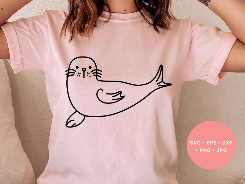 May include: A pink t-shirt with a black line drawing of a seal on the front. The seal is facing left and has a simple, cartoon-like design.