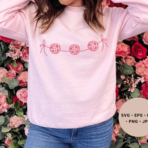 May include: A pink sweatshirt with a graphic of a string of disco balls with pink bows. The text "SVG - EPS - DXF - PNG - JPG" is in the lower right corner of the image.
