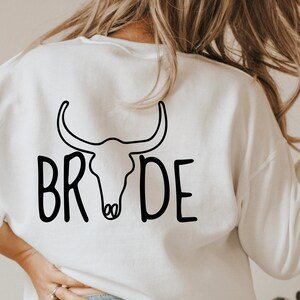 May include: White sweatshirt with a black bull skull graphic and the word "BRIDE" written in a stylized font.