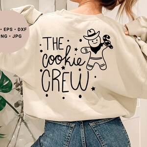 May include: A cream-colored sweatshirt with black text that reads "THE cookie CREW" and a black and white illustration of a gingerbread person wearing a cowboy hat and holding a candy cane.