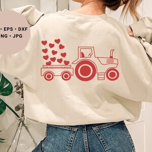 May include: A cream-coloured sweatshirt with a red tractor carrying a bed of red hearts. The text "SVG - EPS - DXF - PNG - JPG" is printed on the left side of the sweatshirt.