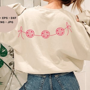 May include: A cream colored sweatshirt with a pink disco ball garland design on the back. The sweatshirt is worn by a person with long brown hair.