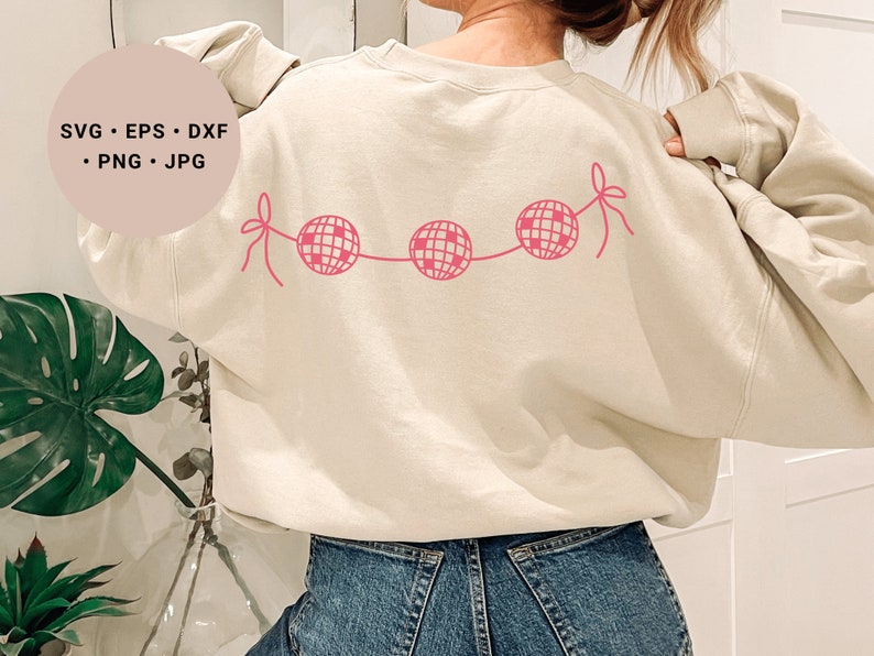 May include: A cream colored sweatshirt with a pink disco ball garland design on the back. The sweatshirt is worn by a person with long brown hair.