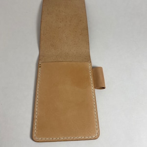 May include: A light brown leather notebook cover with white stitching and a pen holder.