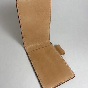 May include: A light brown leather wallet with a flap closure and a pen loop. The wallet is stitched with white thread.