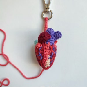 May include: A crocheted heart keyring with a red, pink, purple and teal colour scheme. The heart is attached to a silver keyring.