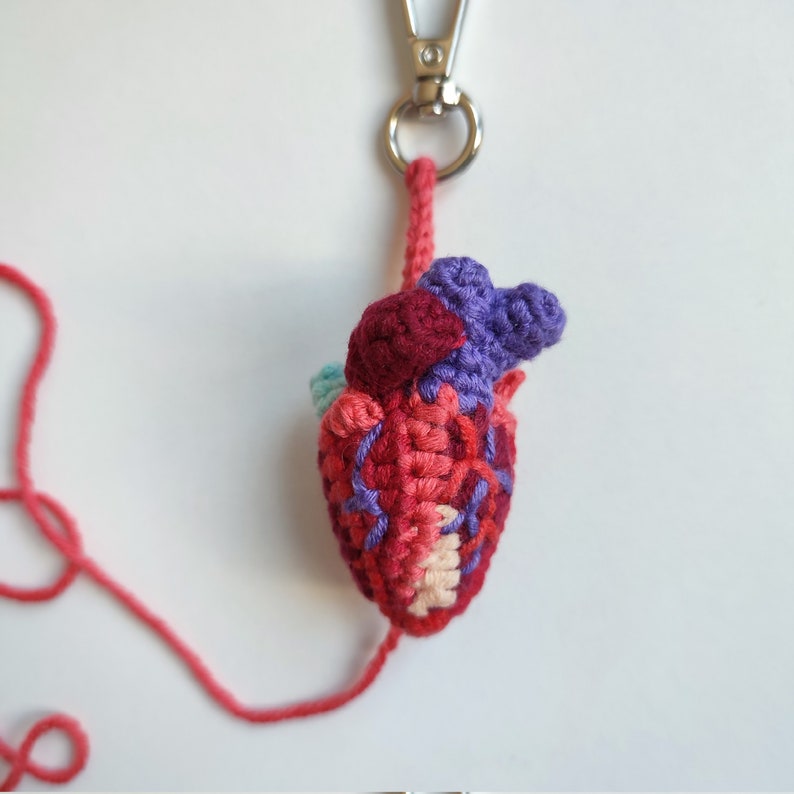 May include: A crocheted heart keyring with a red, pink, purple and teal colour scheme. The heart is attached to a silver keyring.