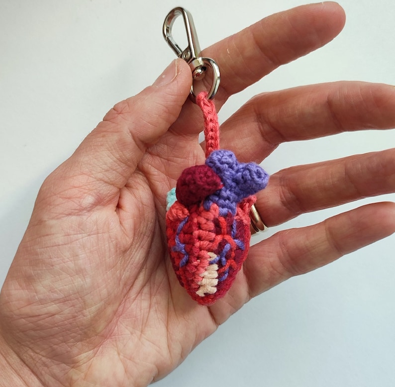May include: A crocheted heart keyring with a silver key ring. The heart is red, pink and purple with a light blue detail.