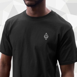 Può includere: Una maglietta nera con un logo bianco di Ethereum in criptovaluta ricamato sul davanti.