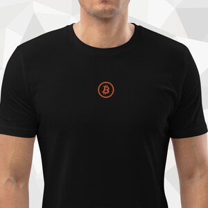 Könnte beinhalten: Ein schwarzes T-Shirt mit einem kleinen, orangefarbenen, gestickten Bitcoin-Logo auf der Vorderseite.