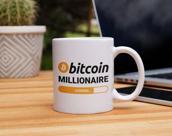 May include: White ceramic mug with a black and yellow design. The mug says "bitcoin millionaire" with a progress bar that says "loading..."