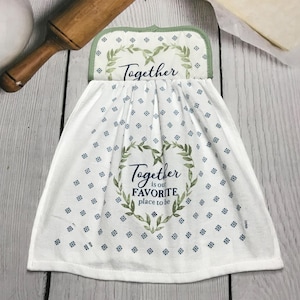 May include: White kitchen towel with a green floral design and the words "Together is our favorite place to be." The towel has a green border and small blue floral accents. A rolling pin is visible in the background.