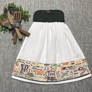 May include: White waffle-weave kitchen towel with a dark green quilted top and a button closure. The bottom border features coffee-themed graphics, including coffee cups, a coffee pot, and text like "I love coffee."