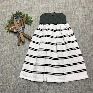May include: A hanging kitchen towel with a dark green quilted top and a white body with black horizontal stripes. A wooden decorative piece with the word "yum" and a small wooden spoon and knife are to the left.