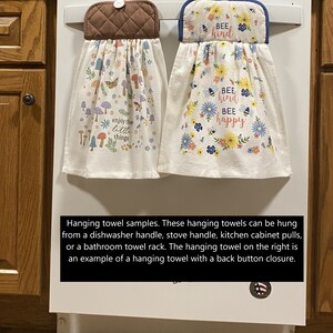May include: Two hanging kitchen towels. One features a brown quilted top with a button, and a white towel with colorful mushrooms, butterflies, and the text "enjoy the little things." The other has a blue-trimmed top with flowers and the text "Bee kind Bee happy."