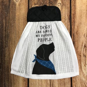 May include: White kitchen towel with a black quilted top and a button. The towel features a black dog silhouette wearing a blue bandana, and the text "DOGS ARE SOME OF MY FAVORITE PEOPLE."
