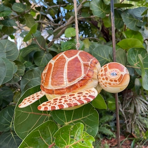May include: A wooden turtle ornament with brown and white painted details. The turtle is hanging from a string and has a realistic appearance.
