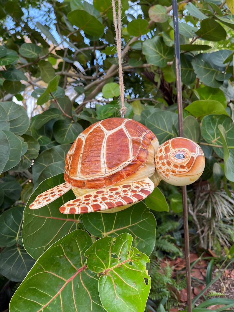 May include: A wooden turtle ornament with brown and white painted details. The turtle is hanging from a string and has a realistic appearance.