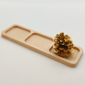 Peut inclure: Un plateau en bois avec trois compartiments, dont l'un contient une pomme de pin peinte en or.