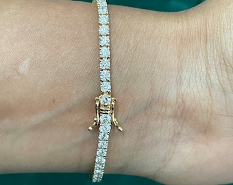 May include: A gold tennis bracelet with a row of clear round stones.