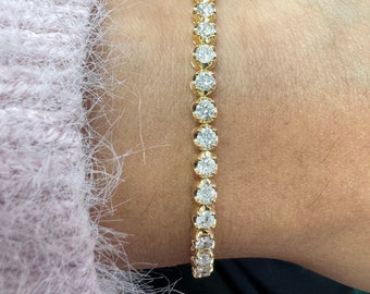May include: A gold tennis bracelet with round diamonds set in a bezel setting.
