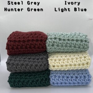 May include: Six crocheted squares stacked on top of each other. The squares are in the following colors from top to bottom: burgundy, steel grey, hunter green, leisure green, ivory, and light blue.