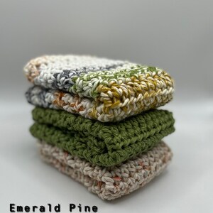 May include: A stack of four crocheted dishcloths in different colors: emerald pine, sage, natural mix, and a multi-colored mix. The dishcloths are made with cotton yarn and are perfect for cleaning dishes and other surfaces.