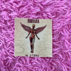 May include: A beige fabric patch with a printed image of a figure with wings, the text "NIRVANA" and "IN UTERO".