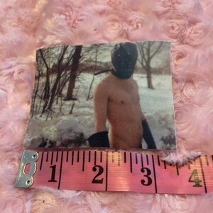 May include: A black and white photo of a person wearing a black mask and standing in a snowy forest. The person is shirtless and has their arms crossed. The photo is printed on a fabric patch.