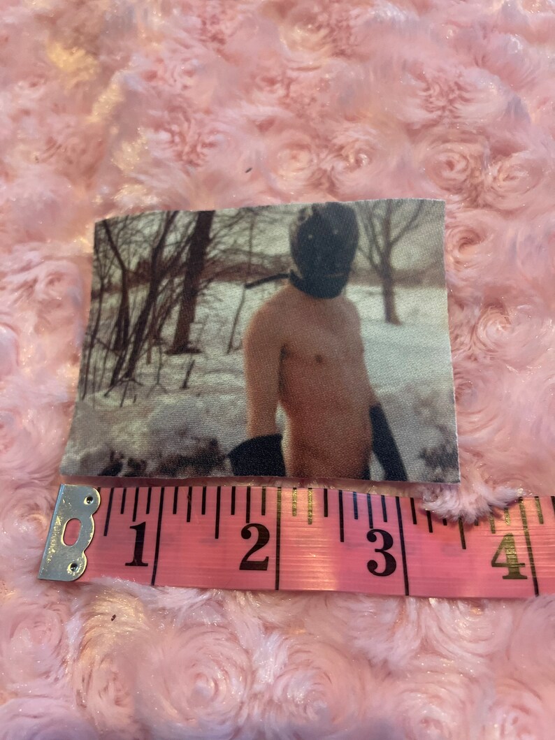 May include: A black and white photo of a person wearing a black mask and standing in a snowy forest. The person is shirtless and has their arms crossed. The photo is printed on a fabric patch.