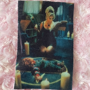 May include: A black and red striped shirt with a white collar and a red bow tie. A doll with a red and white striped shirt and a red bow tie is lying on a pentagram with candles around it. A woman in a black dress is standing over the doll, holding a book and a candle.