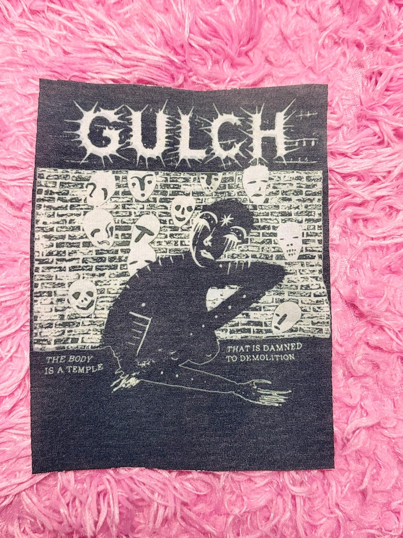 May include: A dark blue patch with the word "GULCH" in white, spiky font. The patch features a black illustration of a figure and skulls, with the phrases "THE BODY IS A TEMPLE" and "THAT IS DAMNED TO DEMOLITION".