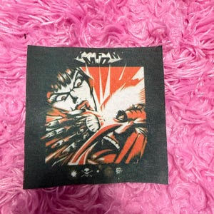 May include: A black square patch with a comic book style illustration. The image features a character with a red and white background, and the word "KRAKEN" at the top. Below the image are three small symbols.