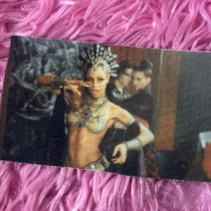 May include: A woman wearing a black and silver costume with a jeweled headpiece and a black feather boa. She is standing in front of a dark background.