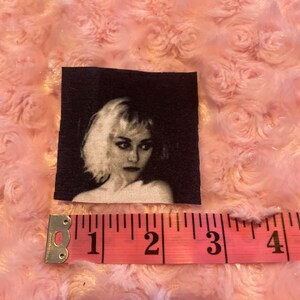 May include: Black and white image of a woman with short, blonde hair. The image is printed on a fabric patch.