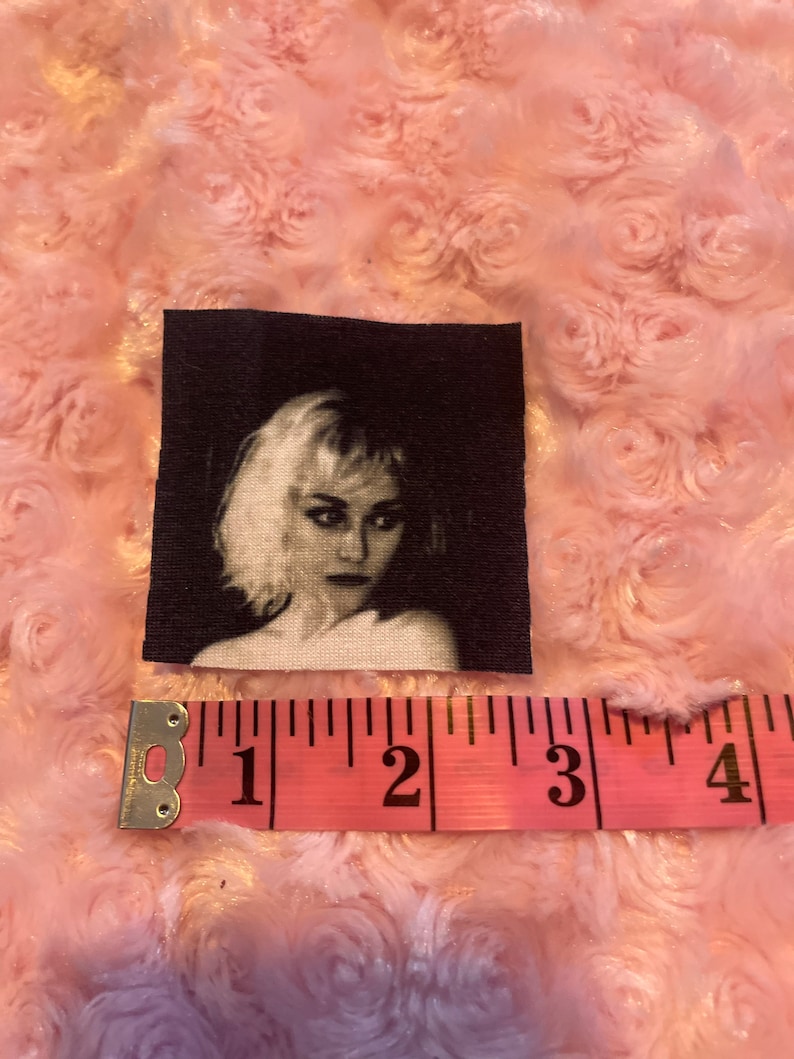 May include: Black and white image of a woman with short, blonde hair. The image is printed on a fabric patch.