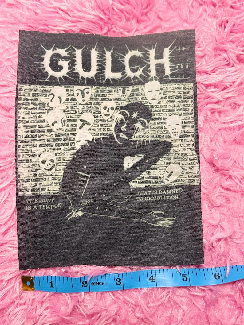 May include: A black and white patch with the word "GULCH" in a spiky font. The patch features a figure, mask designs, and the phrases "THE BODY IS A TEMPLE" and "THAT IS DAMNED TO DEMOLITION". The patch is approximately 10 cm wide.